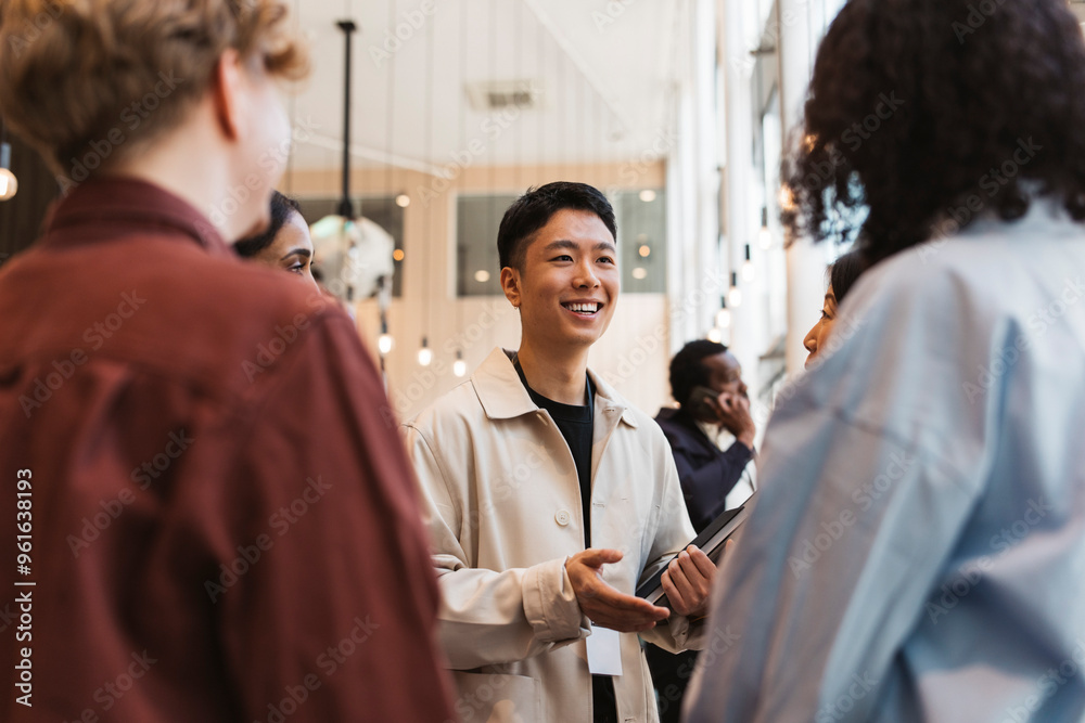 Smiling young male entrepreneur discussing with group of delegates during seminar at convention center Smiling young male entrepreneur discussing with group of delegates during seminar at convention center
