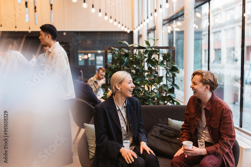 Happy male and female business delegates laughing while sitting on sofa at convention center photo