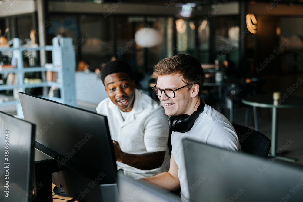 Happy male entrepreneurs watching computer screen while sitting at office Happy male entrepreneurs watching computer screen while sitting at office