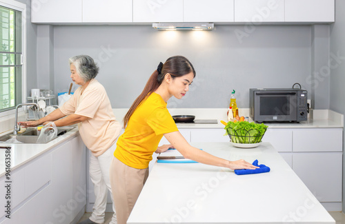 Asian middle aged daughter and senior mother cooking together and cleaning kitchen