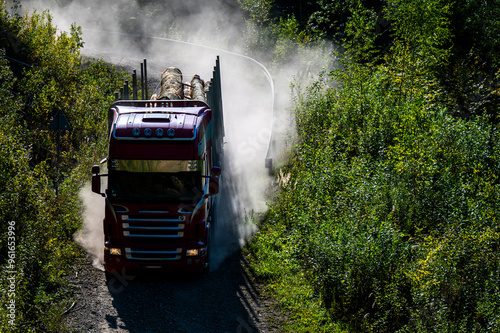 A truck carrying timber on a winding forest road in the mountains.