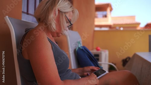 A senior woman with glasses and blonde hair using a vaporizer while relaxing on a patio.