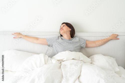 Smiling brunette woman wearing pajama sitting in bed in bedroom