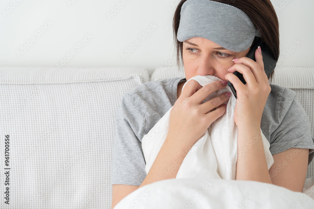 Sad woman wearing sleeping mask using smartphone as she sits in bed covered with duvet Sad woman wearing sleeping mask using smartphone as she sits in bed covered with duvet