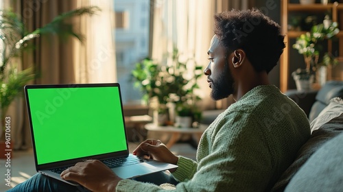 Man Using Laptop with Green Screen in Cozy Living Room
