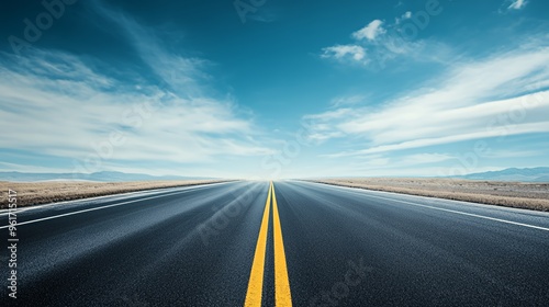Empty asphalt road with double yellow lines, leading to a blue sky with white clouds and distant mountains.