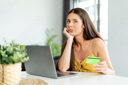 фотографія Contemplative woman holding credit card while online shopping