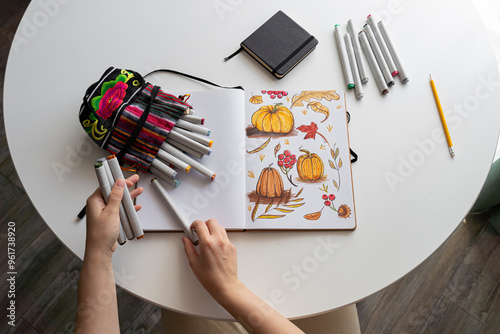 Hand coloring autumn-themed illustration with markers. Top view