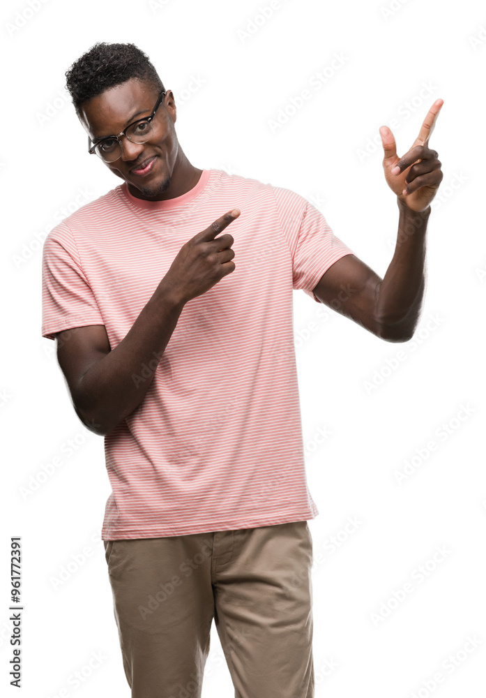 Fototapeta premium Young african american man wearing pink t-shirt smiling and looking at the camera pointing with two hands and fingers to the side.