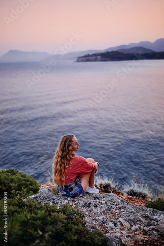 Woman sitting on a rock by the sea at sunset in a coastal location