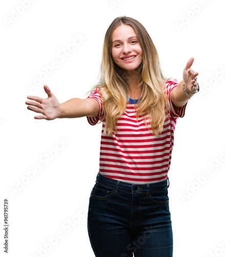 Young beautiful blonde woman over isolated background looking at the camera smiling with open arms for hug. Cheerful expression embracing happiness.