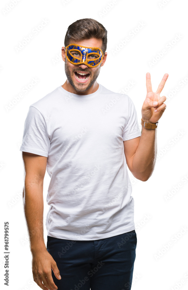 Young handsome man wearing carnival mask over isolated background smiling with happy face winking at the camera doing victory sign. Number two. Young handsome man wearing carnival mask over isolated background smiling with happy face winking at the camera doing victory sign. Number two.