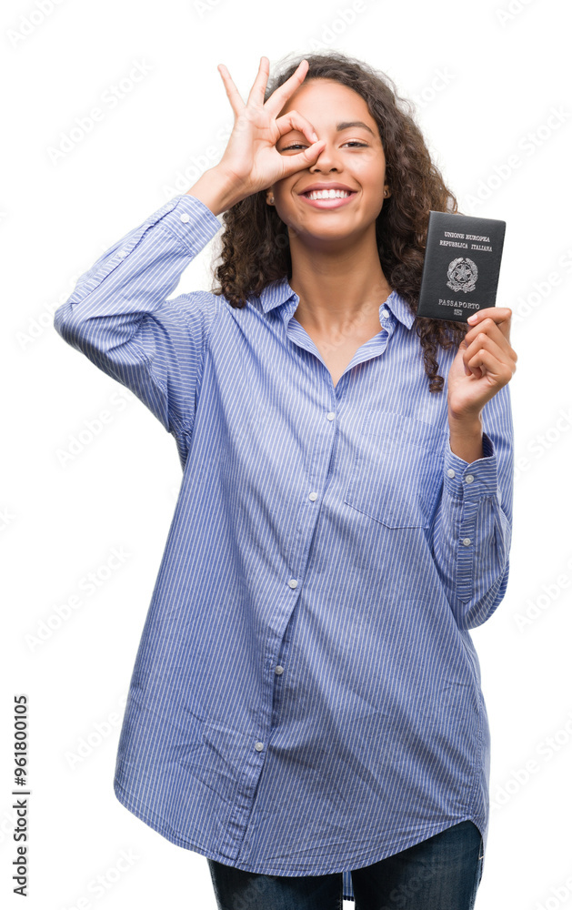 Young hispanic woman holding passport of Italy with happy face smiling doing ok sign with hand on eye looking through fingers Young hispanic woman holding passport of Italy with happy face smiling doing ok sign with hand on eye looking through fingers