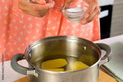 Woman adding salt to water with peeled potatoes cut on halves in saucepan to cook, boil on kitchen at home. Cuisine, culinary, prepare cook domestic food, recipe, raw vegetables ingredients, products.