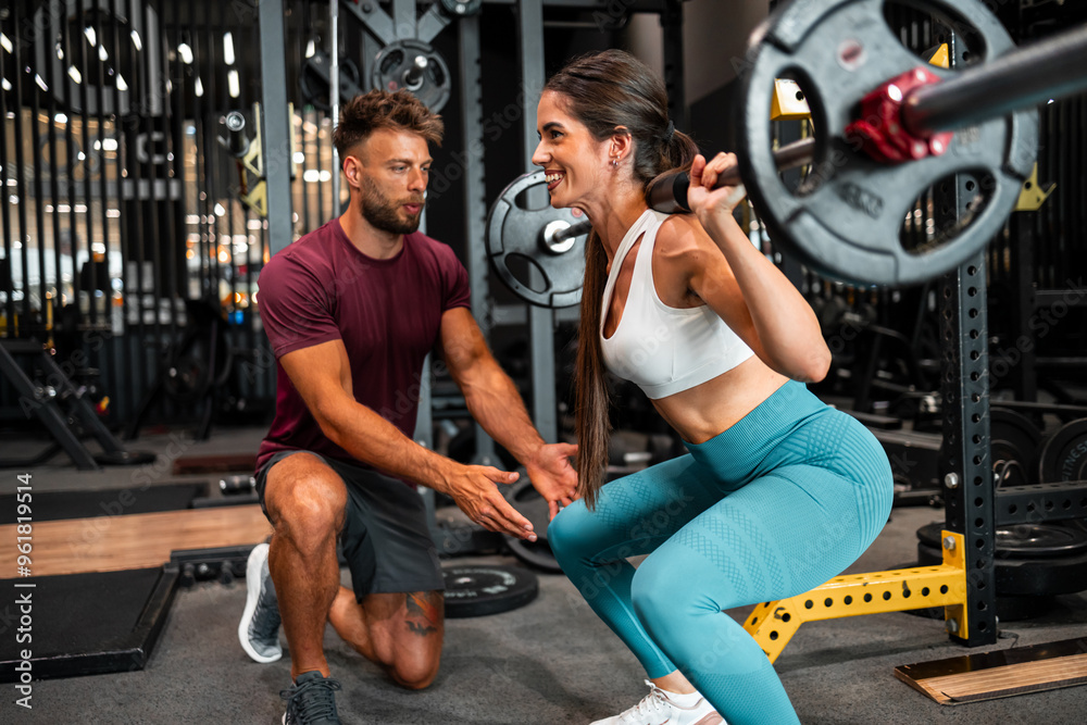 A happy female trainee lifting weight at the gym with the help of her male coach