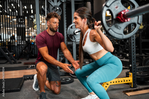 Obraz na płótnie A happy female trainee lifting weight at the gym with the help of her male coach w salonie