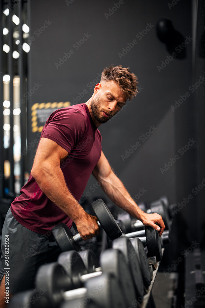 A fit young adult man working out at the gym with a dumbbell A fit young adult man working out at the gym with a dumbbell
