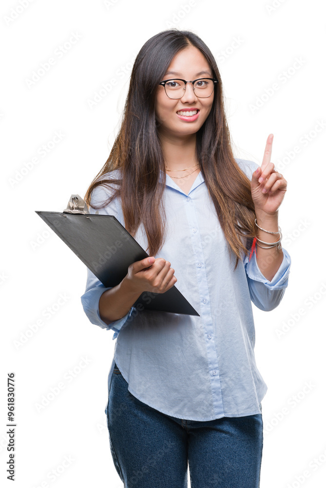 Young asian business woman holding clipboard over isolated background surprised with an idea or question pointing finger with happy face, number one Young asian business woman holding clipboard over isolated background surprised with an idea or question pointing finger with happy face, number one