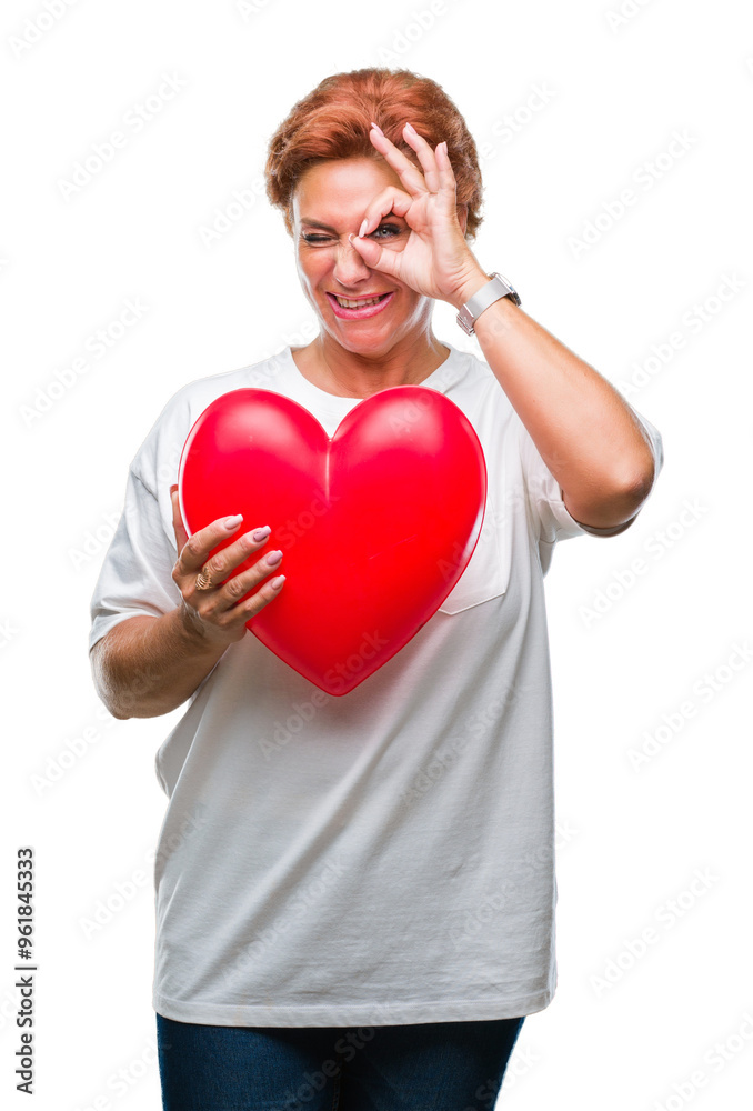 Senior caucasian woman holding red heart in love over isolated background with happy face smiling doing ok sign with hand on eye looking through fingers Senior caucasian woman holding red heart in love over isolated background with happy face smiling doing ok sign with hand on eye looking through fingers