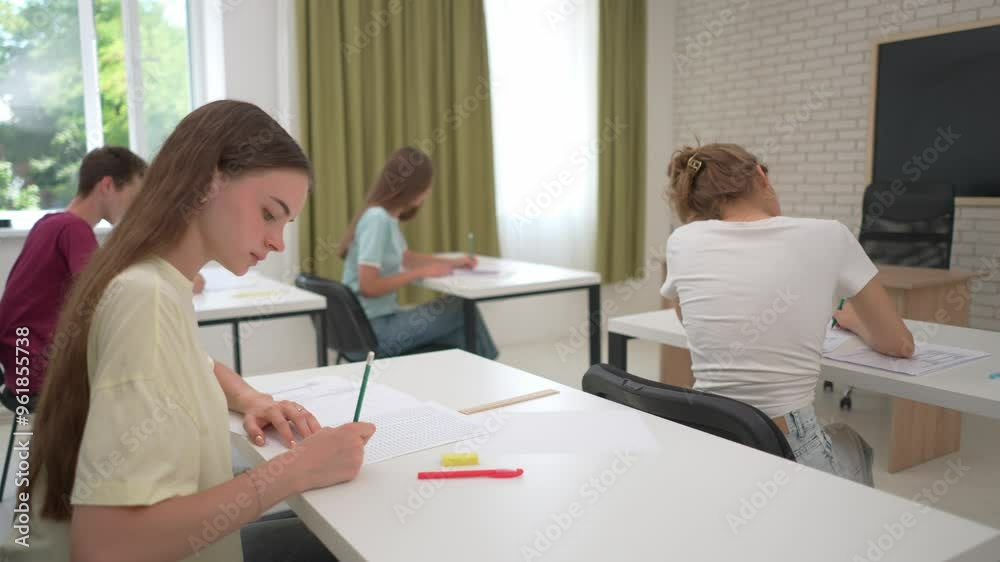 High school teenagers in classroom sitting at desks finishing writing exam after time up bell, talking having break. Modern education concept. High school teenagers in classroom sitting at desks finishing writing exam after time up bell, talking having break. Modern education concept.