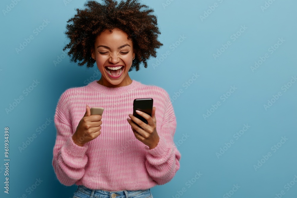 A full-size photo of a pretty young woman in a pullover with her hand raised on a teal background showing her using her phone and raising her fist A full-size photo of a pretty young woman in a pullover with her hand raised on a teal background showing her using her phone and raising her fist