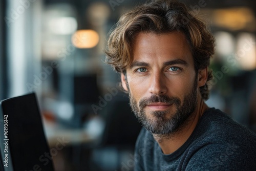 A man with a beard and glasses is sitting in front of a laptop