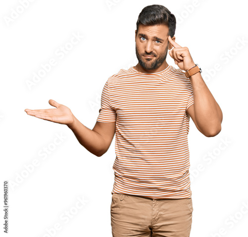 Handsome hispanic man wearing casual clothes confused and annoyed with open palm showing copy space and pointing finger to forehead. think about it.