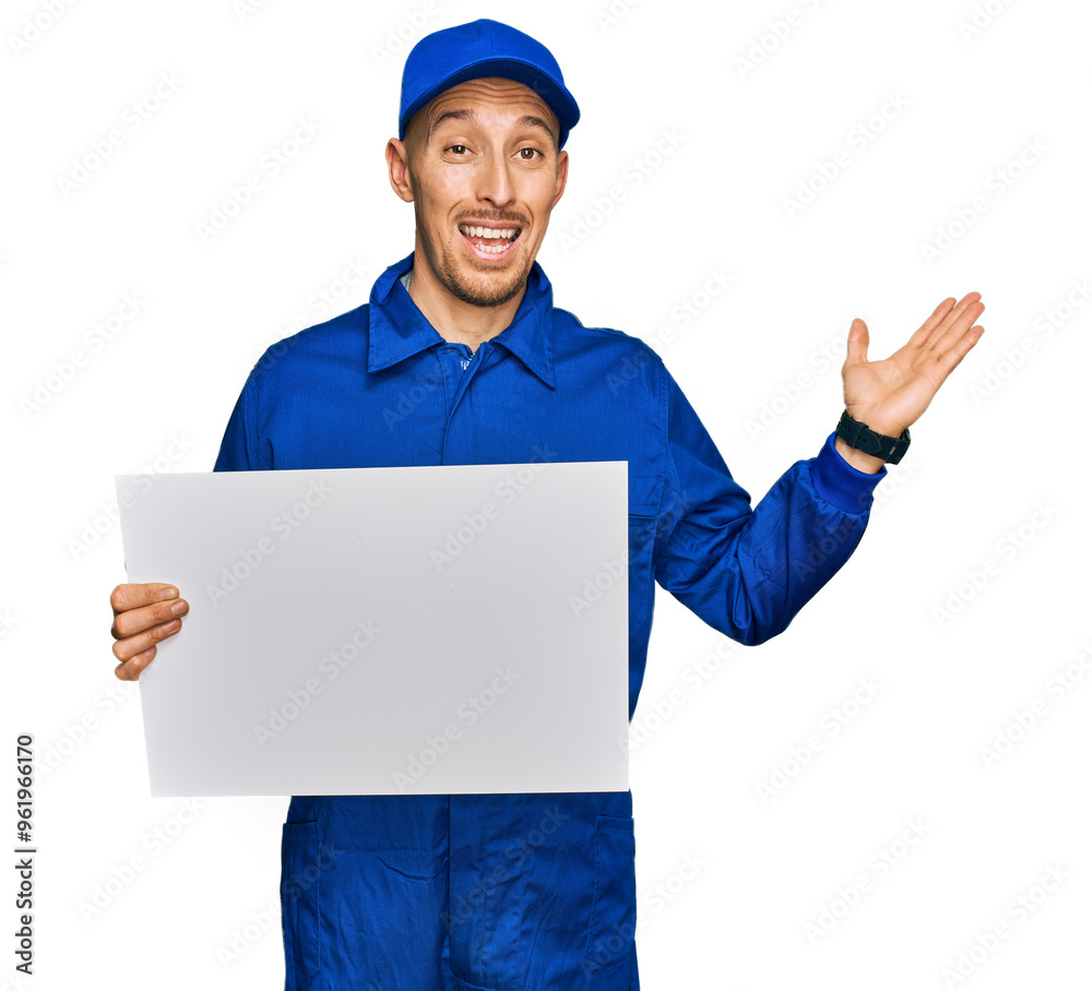 Bald man with beard wearing builder jumpsuit uniform holding empty banner celebrating victory with happy smile and winner expression with raised hands Bald man with beard wearing builder jumpsuit uniform holding empty banner celebrating victory with happy smile and winner expression with raised hands