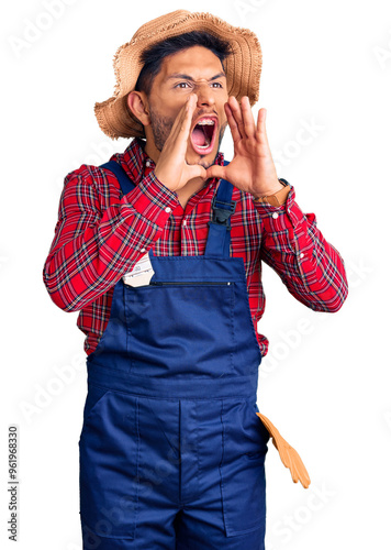 Handsome latin american young man weaing handyman uniform shouting angry out loud with hands over mouth photo