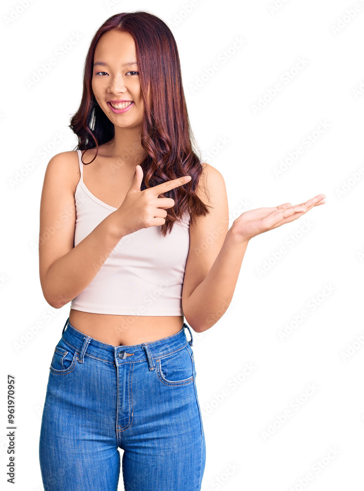 Young beautiful chinese girl wearing casual clothes amazed and smiling to the camera while presenting with hand and pointing with finger. Young beautiful chinese girl wearing casual clothes amazed and smiling to the camera while presenting with hand and pointing with finger.