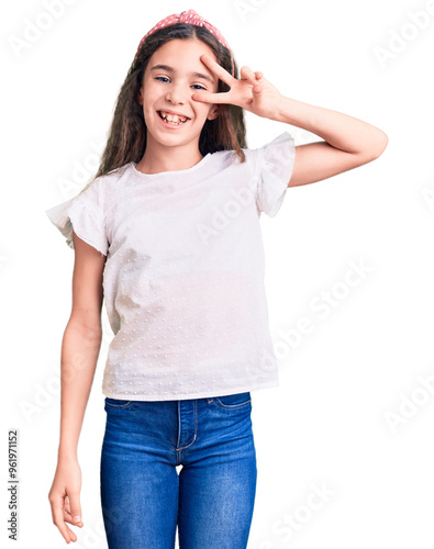 Cute hispanic child girl wearing casual white tshirt doing peace symbol with fingers over face, smiling cheerful showing victory