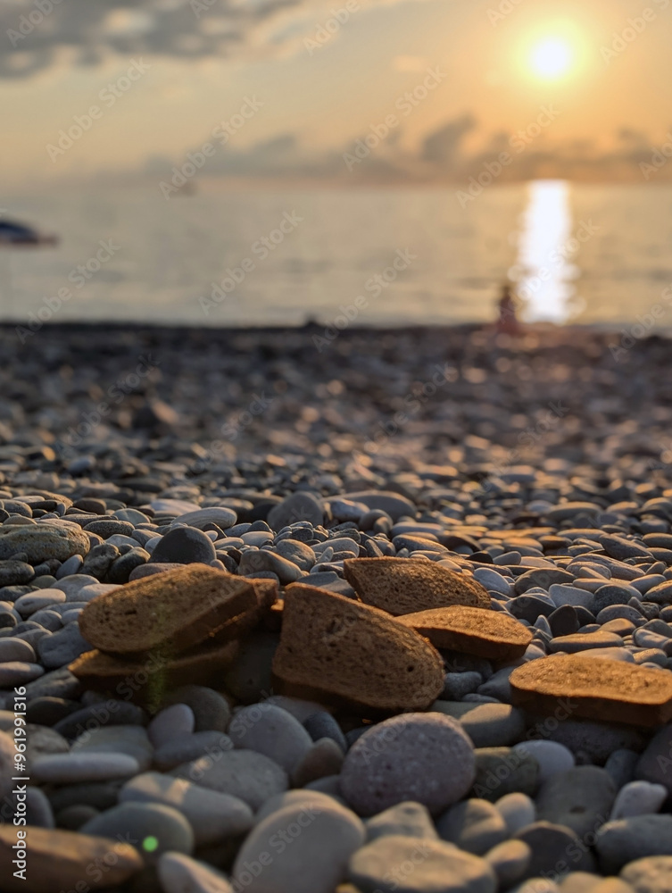 Obraz premium Pieces of black bread scattered on the beach. Against the background of the sunset. Trash and garbage.