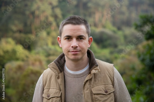 Man in vest, nature background. A young man wearing a brown vest, standing in front of a blurred green background, conveying a sense of calmness and peace.