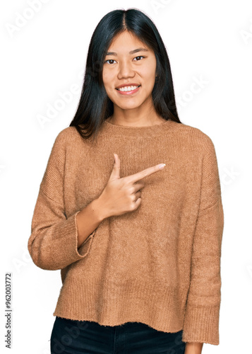 Beautiful young asian woman wearing casual winter sweater cheerful with a smile of face pointing with hand and finger up to the side with happy and natural expression on face