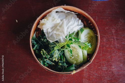 A bowl of fresh vegetables including cucumbers and greens on a wooden table. photo