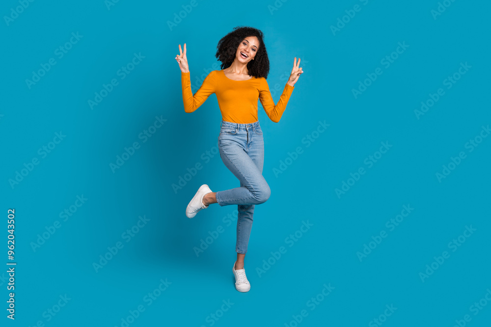 Full body photo of attractive young woman show v-sign dressed stylish yellow clothes isolated on blue color background Full body photo of attractive young woman show v-sign dressed stylish yellow clothes isolated on blue color background