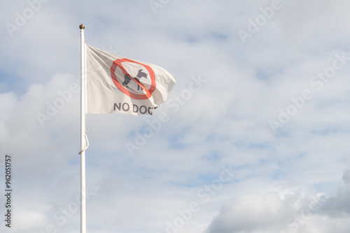 No Dogs flag flying in wind with blue sky and white clouds behind