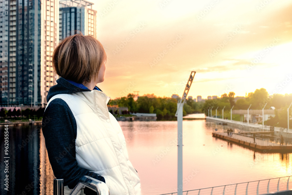 Fototapeta premium A woman on the embankment of the river in the city looks at the sunset. Kyiv, Rivermall park
