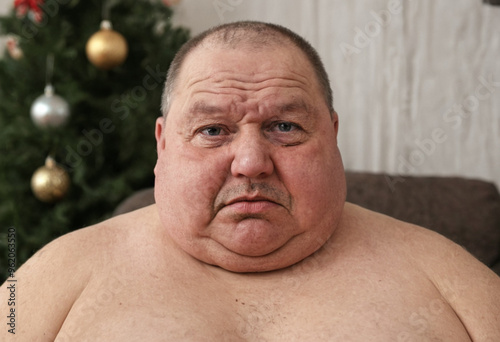 Overweight man, 50-60, sweating in warm winter temperatures, sitting by Christmas tree, single and divorced, reflecting on life during holidays.