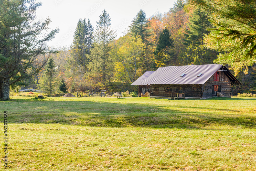 Obraz premium Old wooden barns in a meadow at the foot of a forested hill on a sunny autumn day