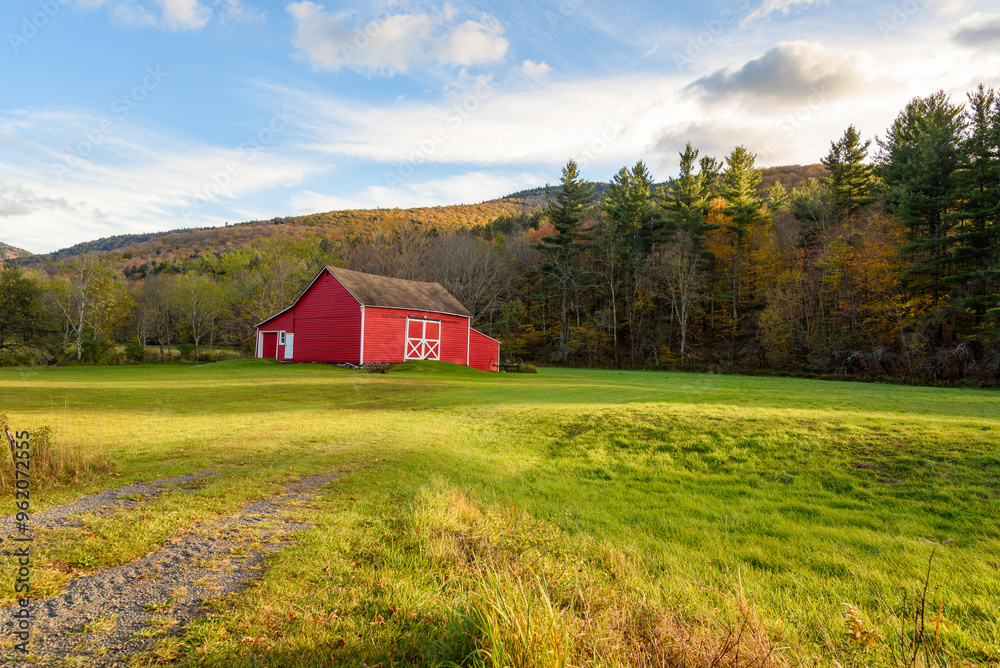 Traditional red American wooden barn in field at the foot of a forested mountain at sunset in autumn Traditional red American wooden barn in field at the foot of a forested mountain at sunset in autumn