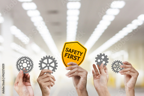 Hand holding safety first symbols and holding gear from at warehouse background.