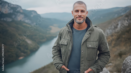 A rugged man stands confidently against a stunning natural backdrop, embodying adventure in his casual attire, with a serene lake and lush mountains framing the scene