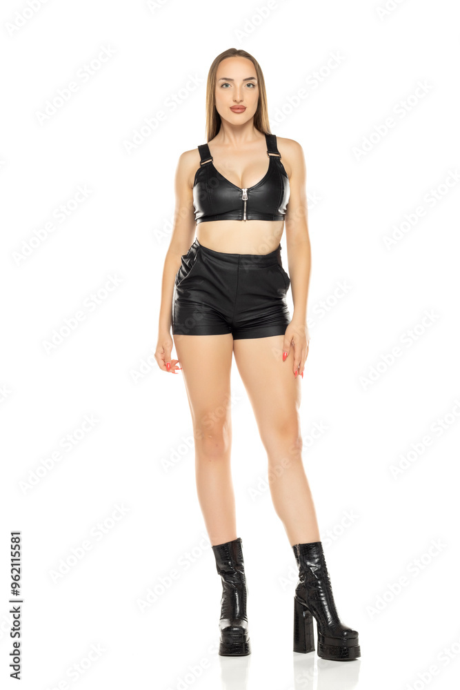 Beautiful blond woman in leather shorts, bra and boots on a white background. Front view. Beautiful blond woman in leather shorts, bra and boots on a white background. Front view.