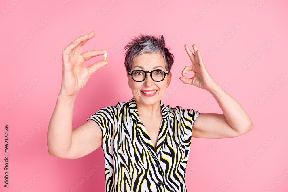 Photo of nice aged woman hold pill show okey symbol wear zebra print shirt isolated on pink color background Photo of nice aged woman hold pill show okey symbol wear zebra print shirt isolated on pink color background