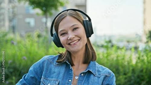 Portrait of beautiful smiling young woman in headphones looking at camera, outdoors