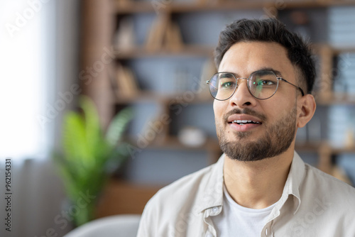 Hispanic man with glasses at home looking content and thoughtful in modern indoor setting