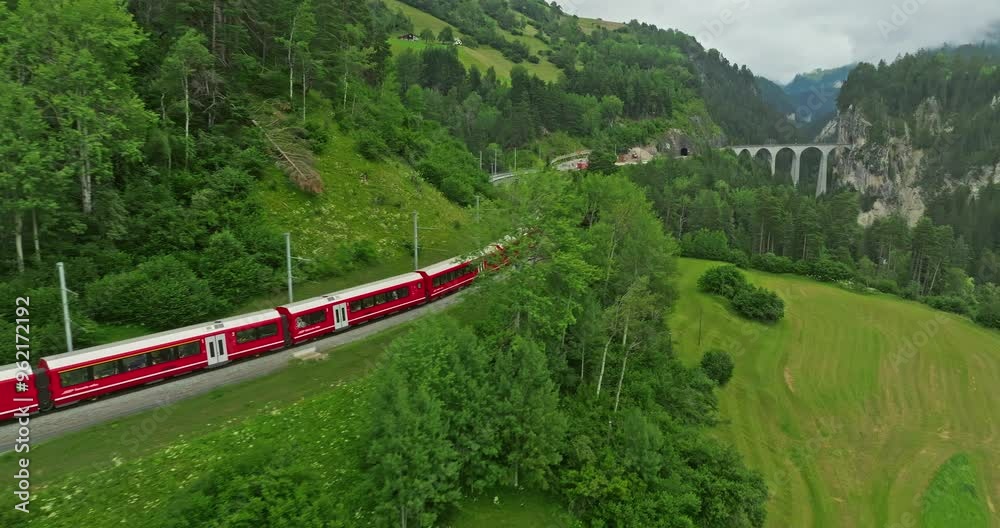 Aerial drone shot red train passing through famous mountain in Filisur, Switzerland. Drone footage of train traveling between mountains in Swiss countryside, Swiss mountain. Aerial drone Switzerland