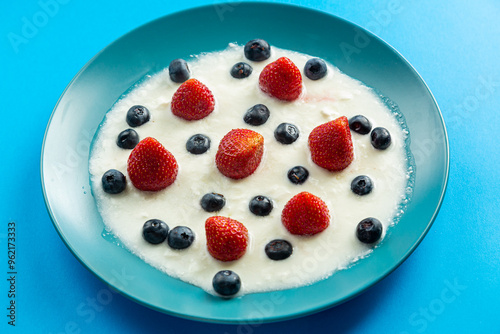 Berries juicy strawberries and blueberries in a blue plate with cream on a blue background, top view