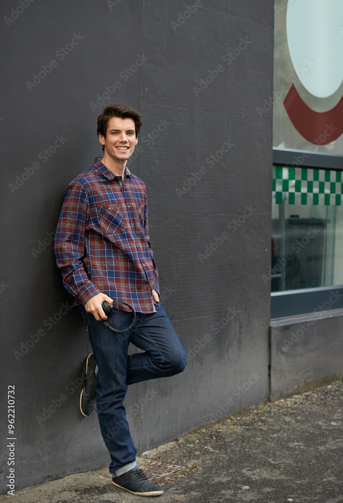 Wall background, happy and portrait of man in city with fashion, trendy clothes and casual outfit. Urban town, relax and person with headphones for music, audio and podcast in street on weekend Wall background, happy and portrait of man in city with fashion, trendy clothes and casual outfit. Urban town, relax and person with headphones for music, audio and podcast in street on weekend